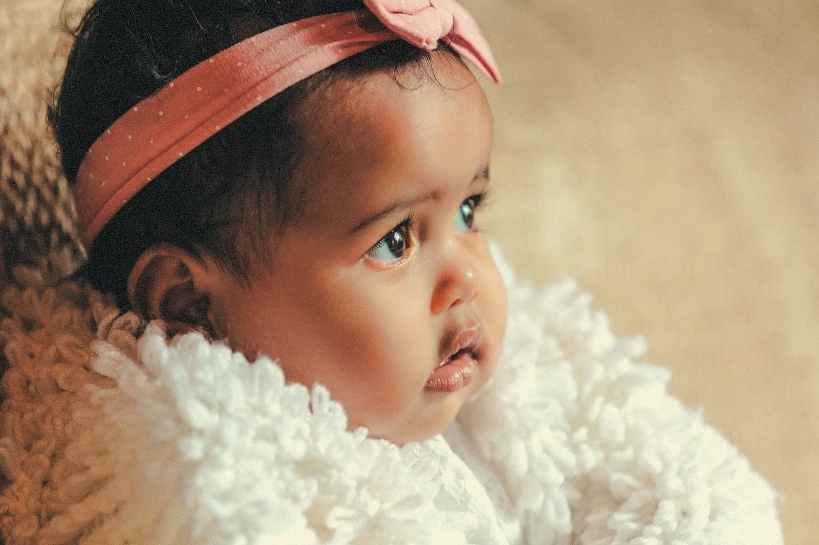 A baby girl with a pink bow headband, looking up
