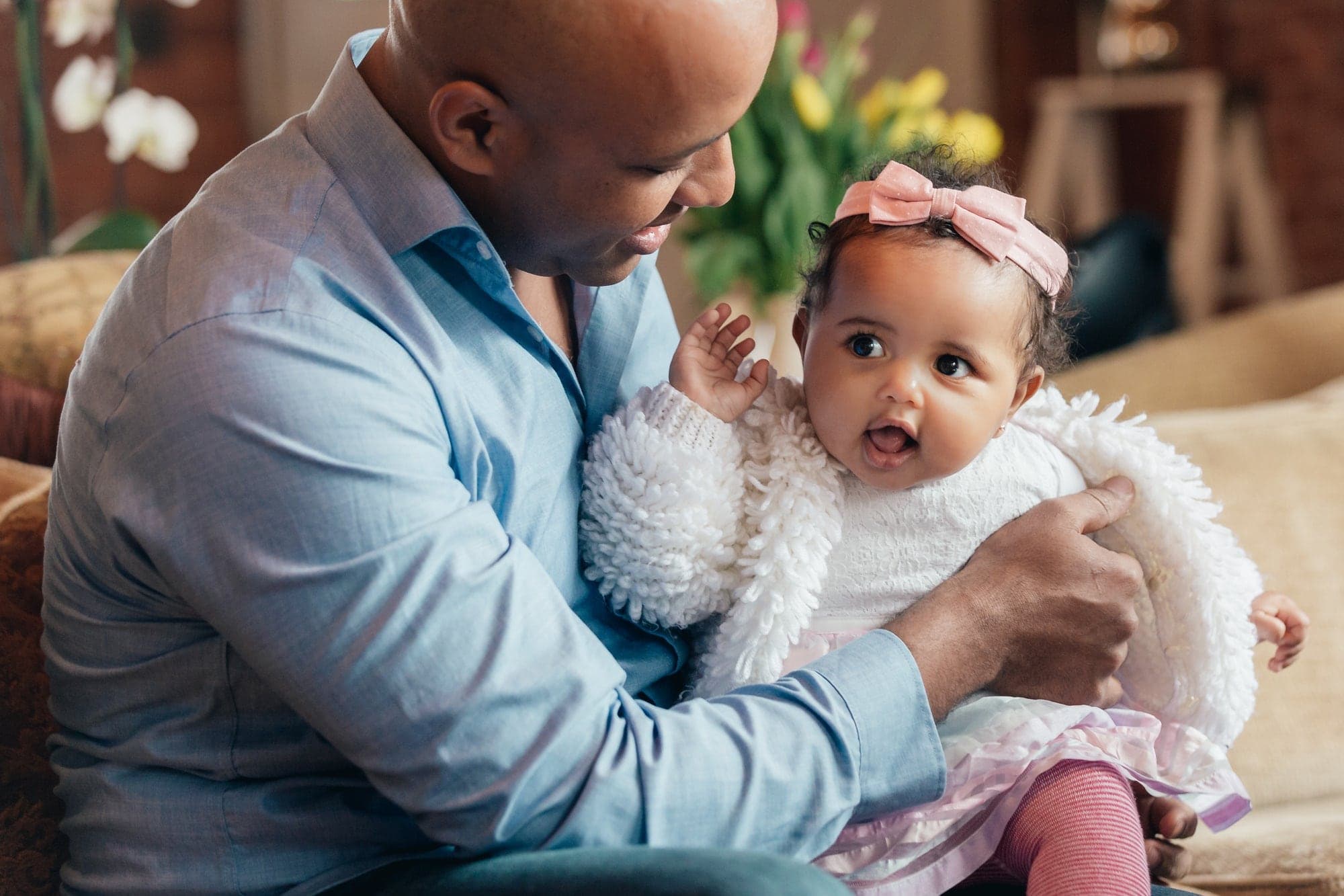 A father holding his baby girl on the sofa, both looking up