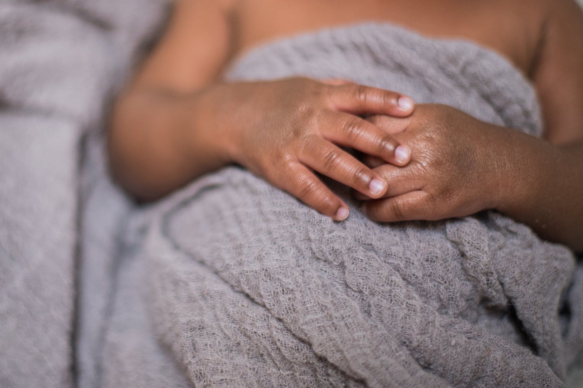 A newborn's hands resting on a grey knitted blanket