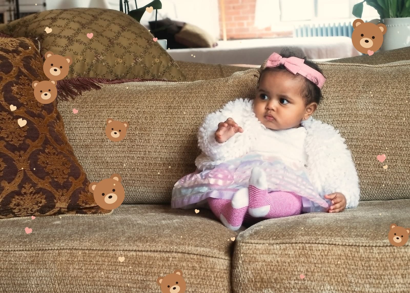 A baby girl on the sofa in Teddy Bear World, tiny bears and hearts around